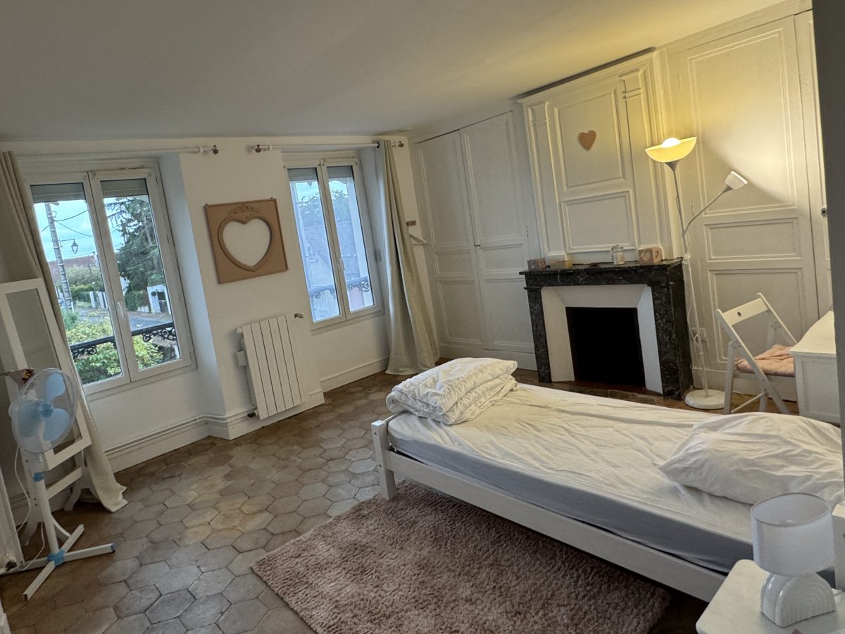 La seconde chambre après travaux : cheminée de marbre décorative, tommettes, lit simple et murs blancs