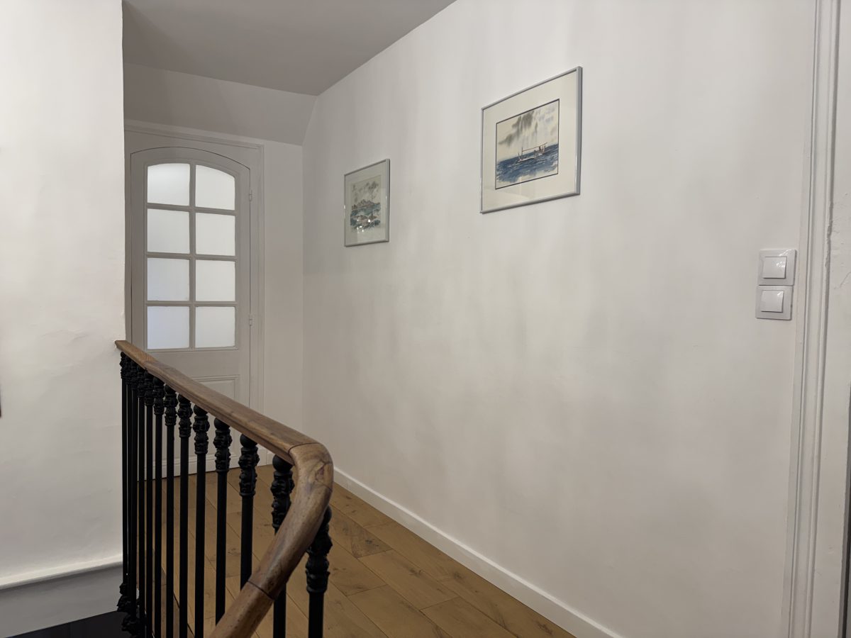 Le palier après travaux : murs blancs, parquet posé, balustrade en fonte conservée