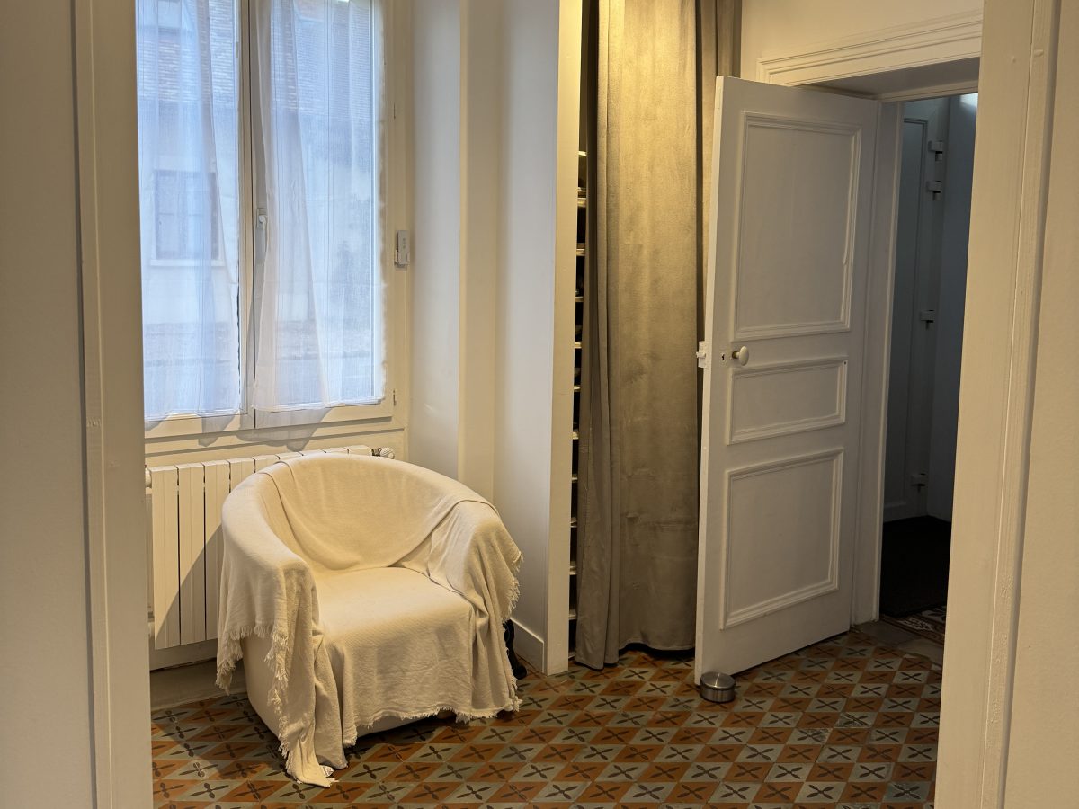 Le vestiaire après travaux : carreaux de ciment anciens, fauteuil et penderie fermée par un rideau